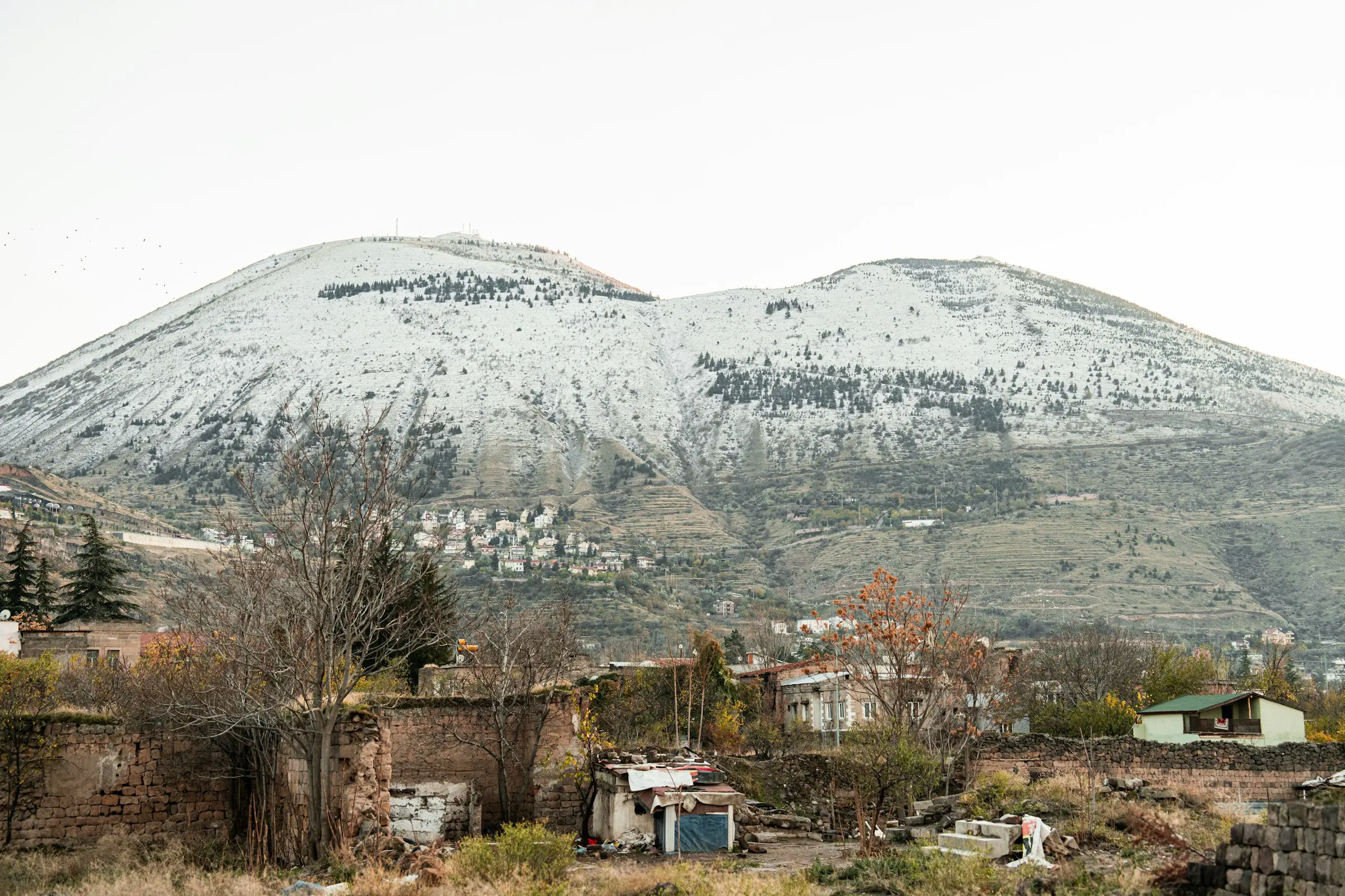 Snow-covered mountain landscape with small houses and trees in the foreground, seen at the base of Mount Erciyes.