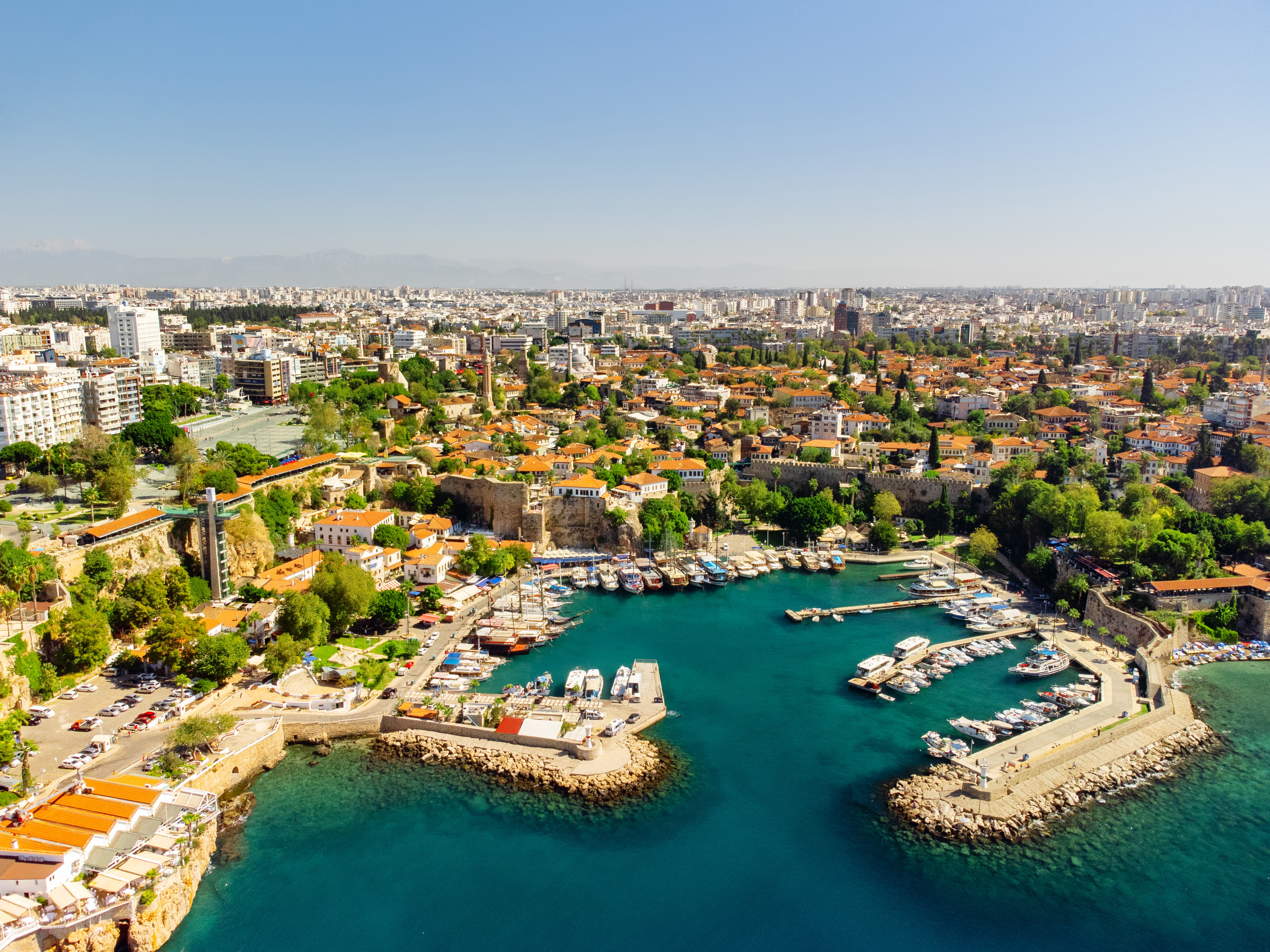 Utsikt over gamlebyen i Antalya, Tyrkia med historiske bygninger, grønn vegetasjon, og en travel marina med båter ved det turkise vannet