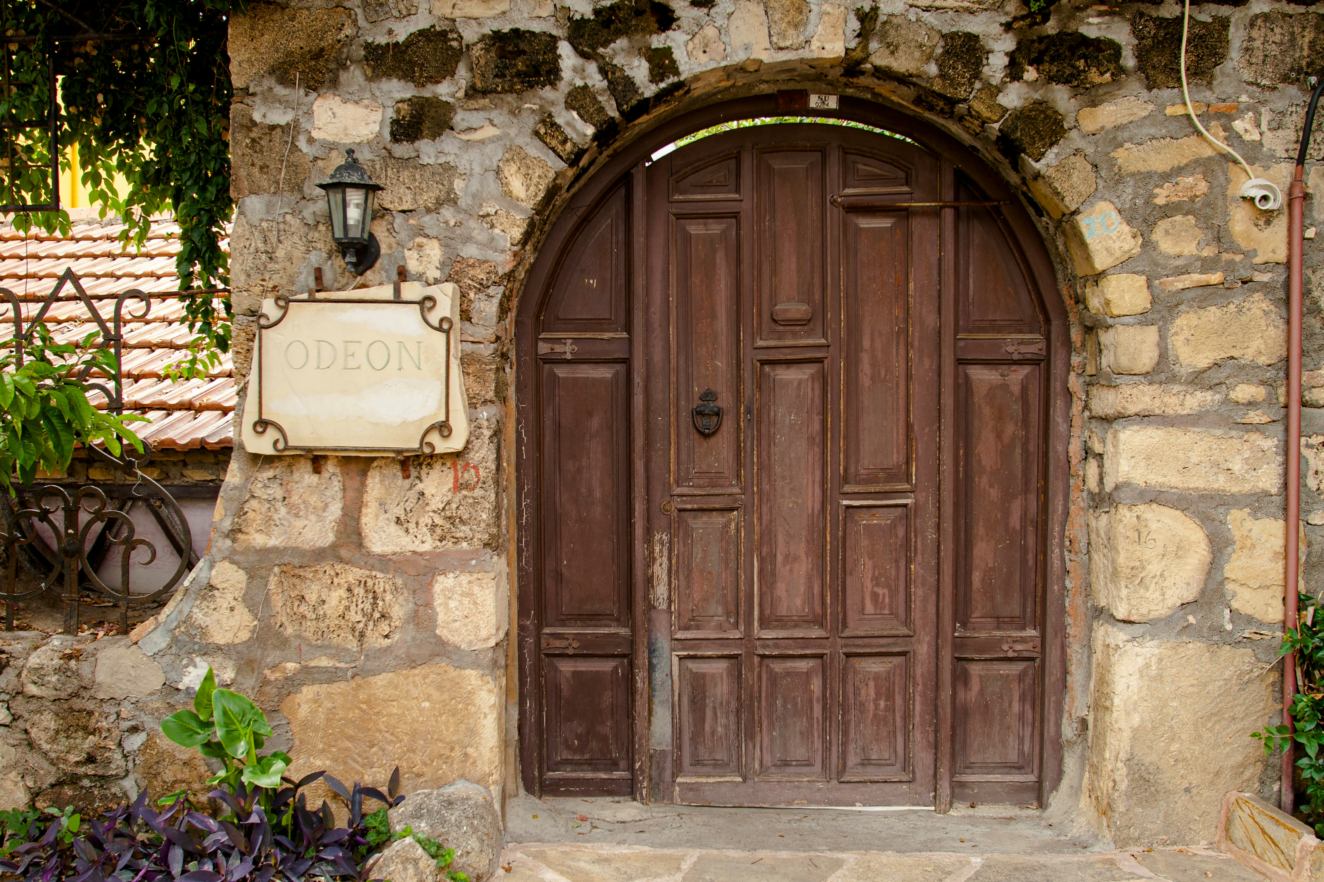 Rustikk trebue med skiltet "Odeon" og steinvegg, omgitt av grønn vegetasjon, tradisjonell arkitektur