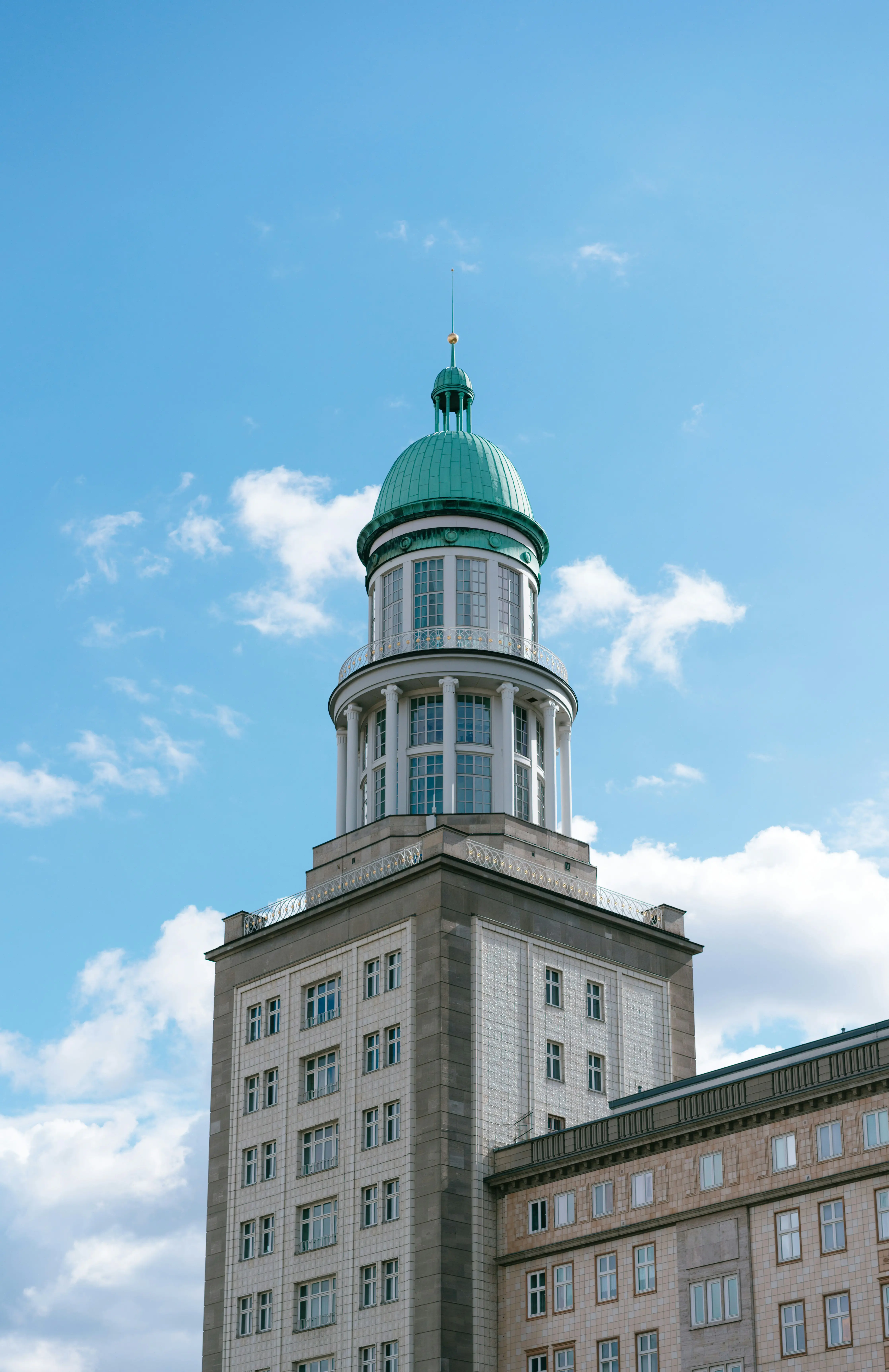 Historisk bygning med grønn kuppel mot blå himmel og skyer, med klassisk arkitektur og flere vinduer