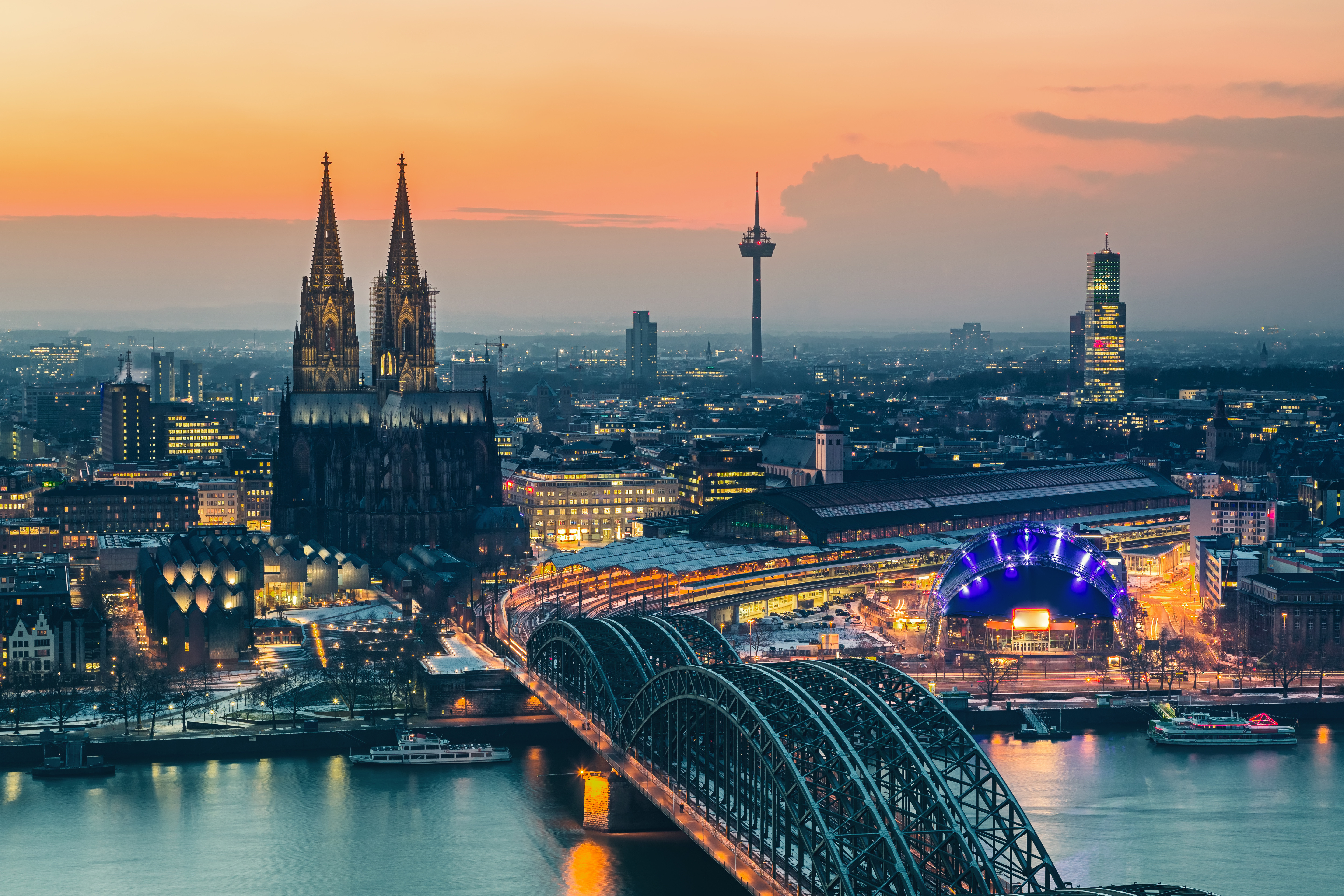Cologne cityscape at sunset featuring the Cologne Cathedral, illuminated bridges, and the Rhine River