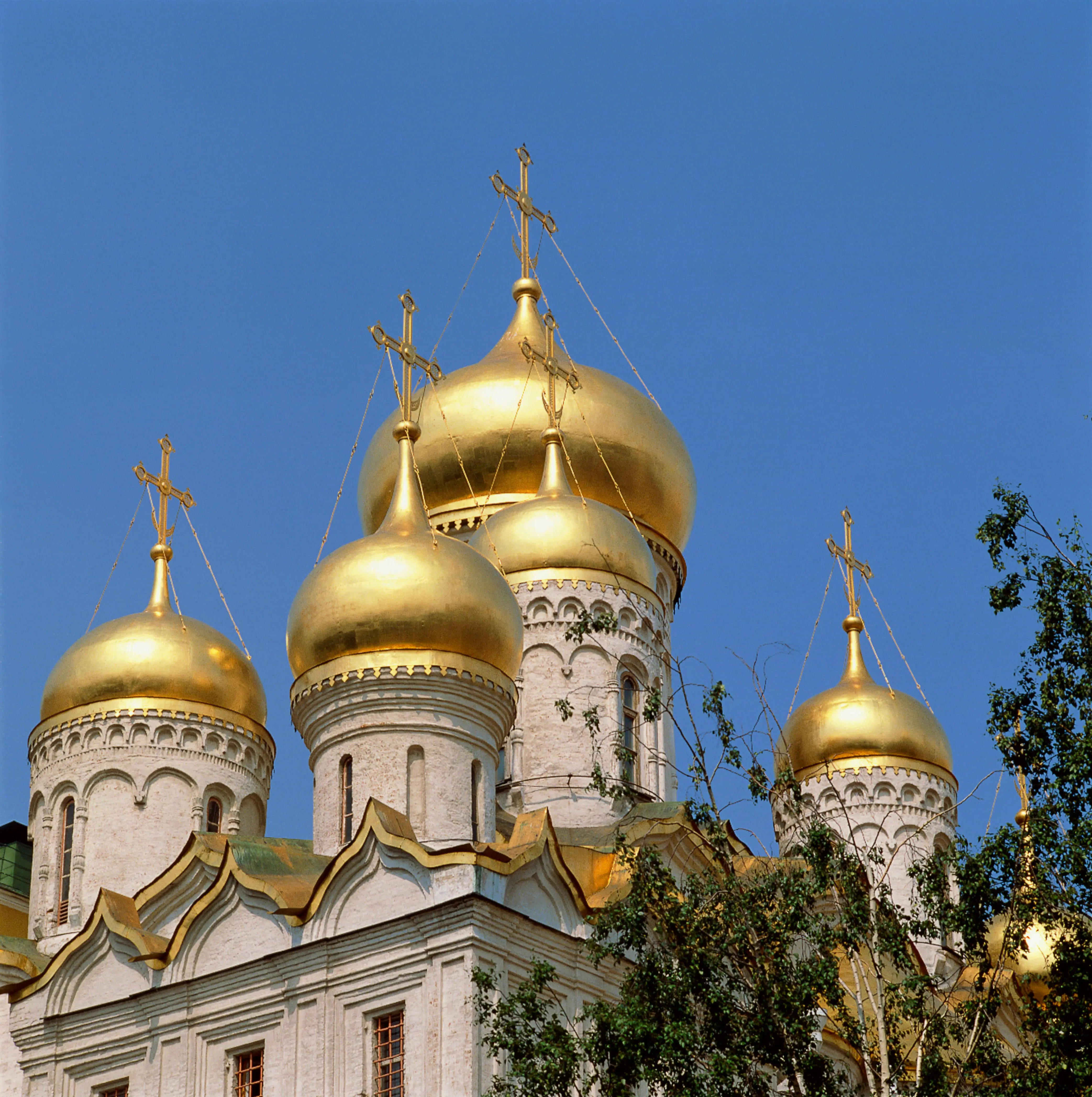 Gylne kupler av en russisk-ortodoks kirke mot en klar blå himmel, med utsmykkede kors og detaljerte arkitektoniske elementer
