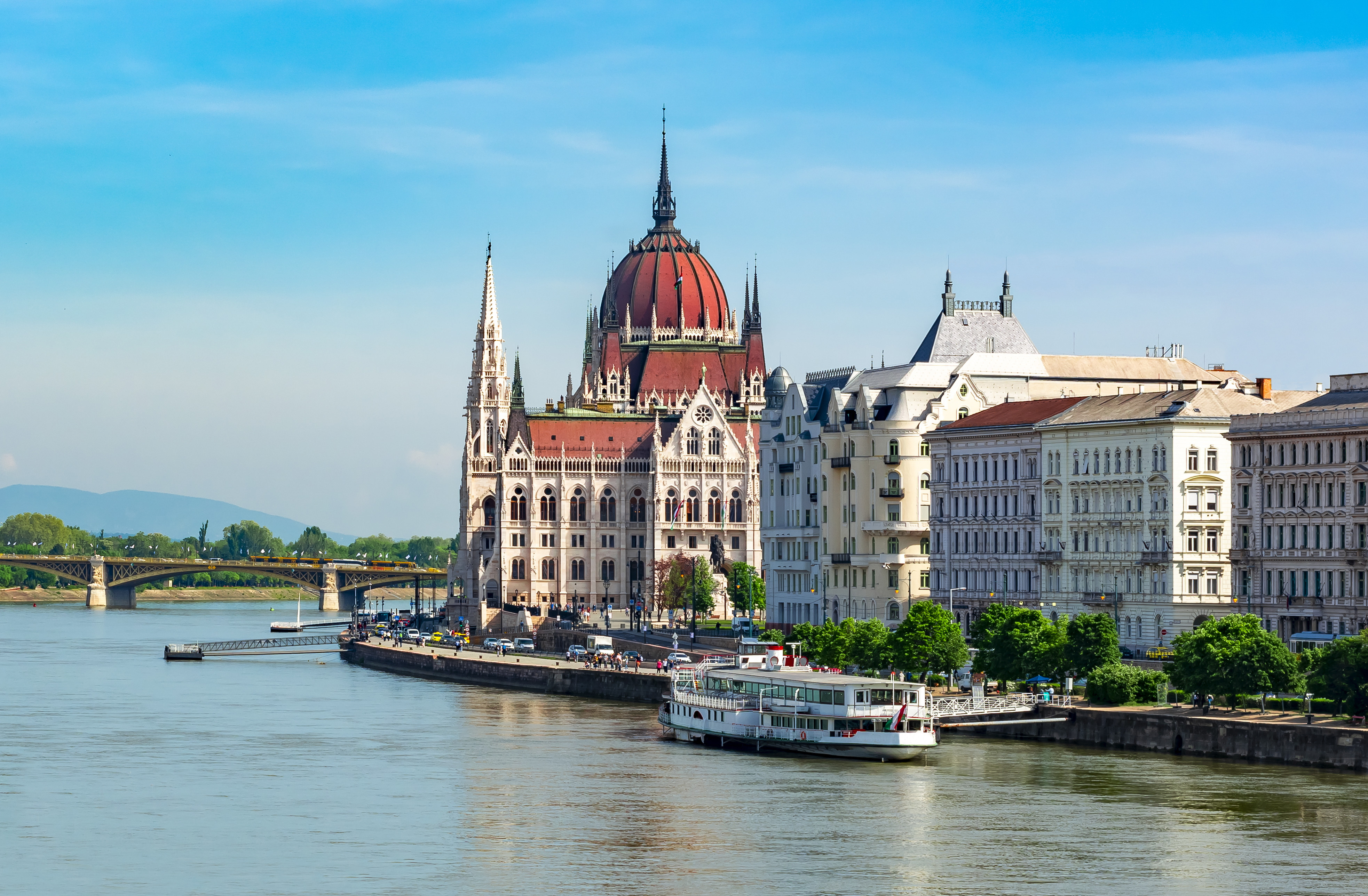Parlamentet i Budapest ved elven Donau en solrik dag, med klassiske bygninger og sightseeingbåt