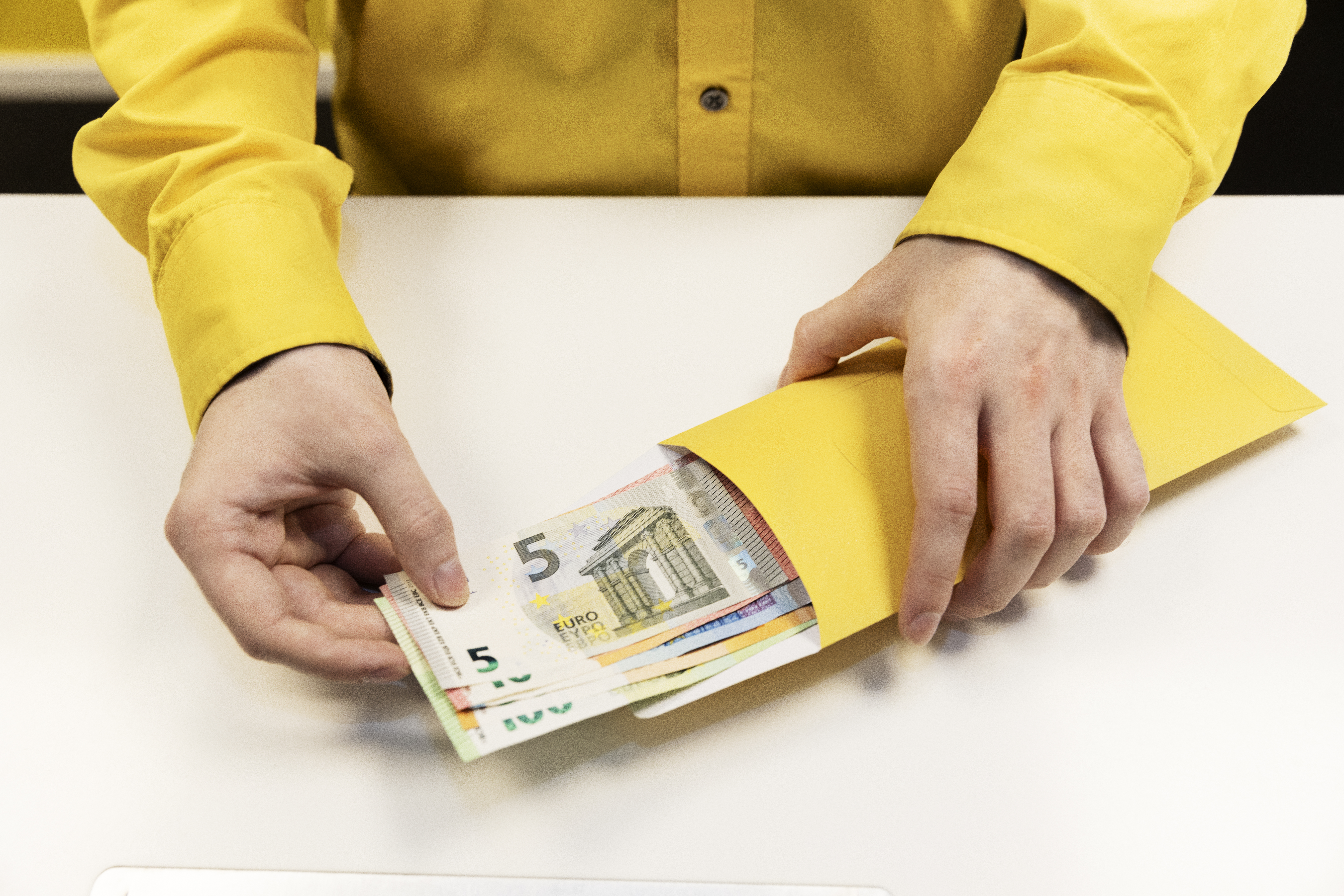 Person in yellow shirt withdraws travel currency, euro banknotes from a yellow envelope.