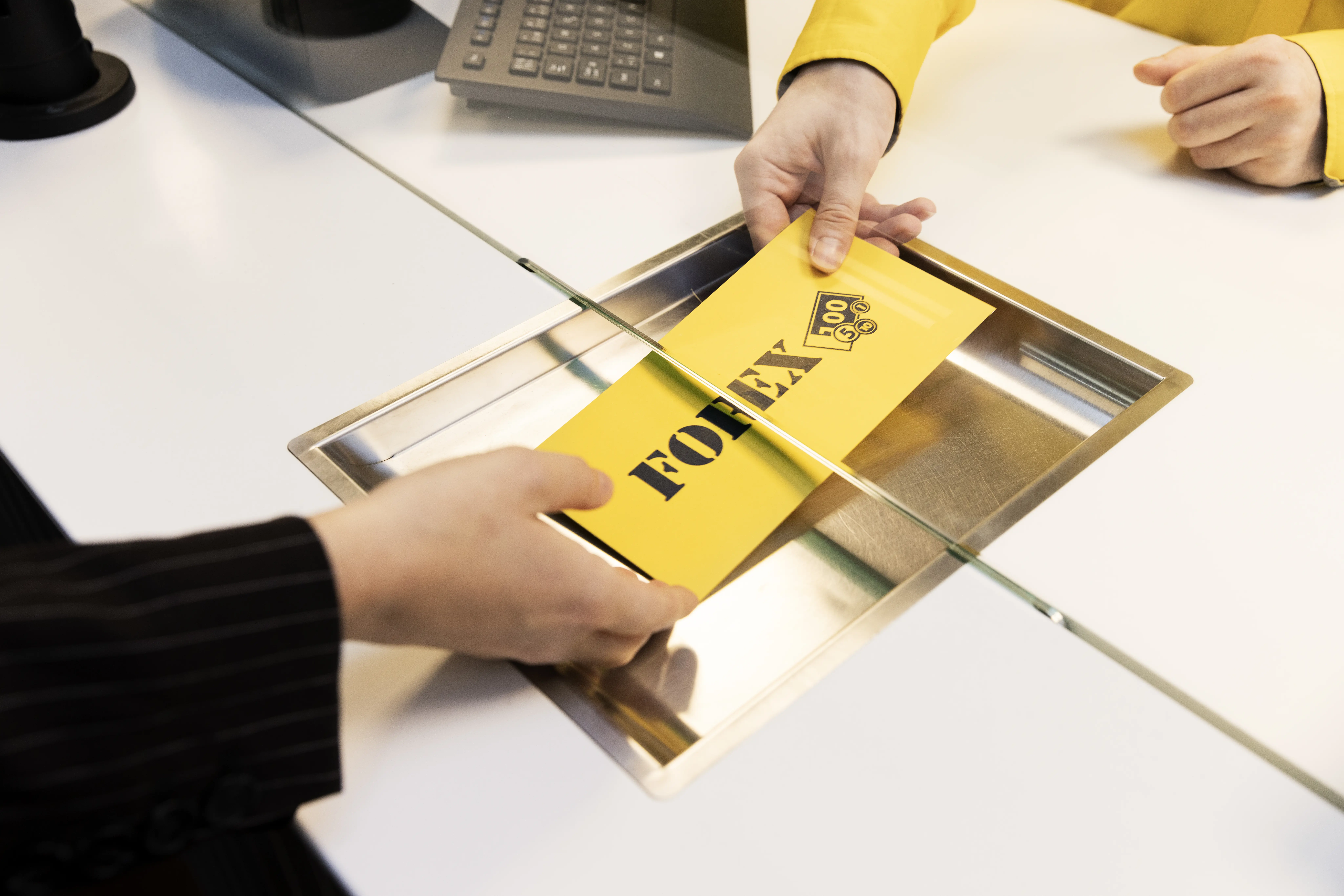 Person handing a yellow envelope labeled "Forex" through a financial transaction counter.