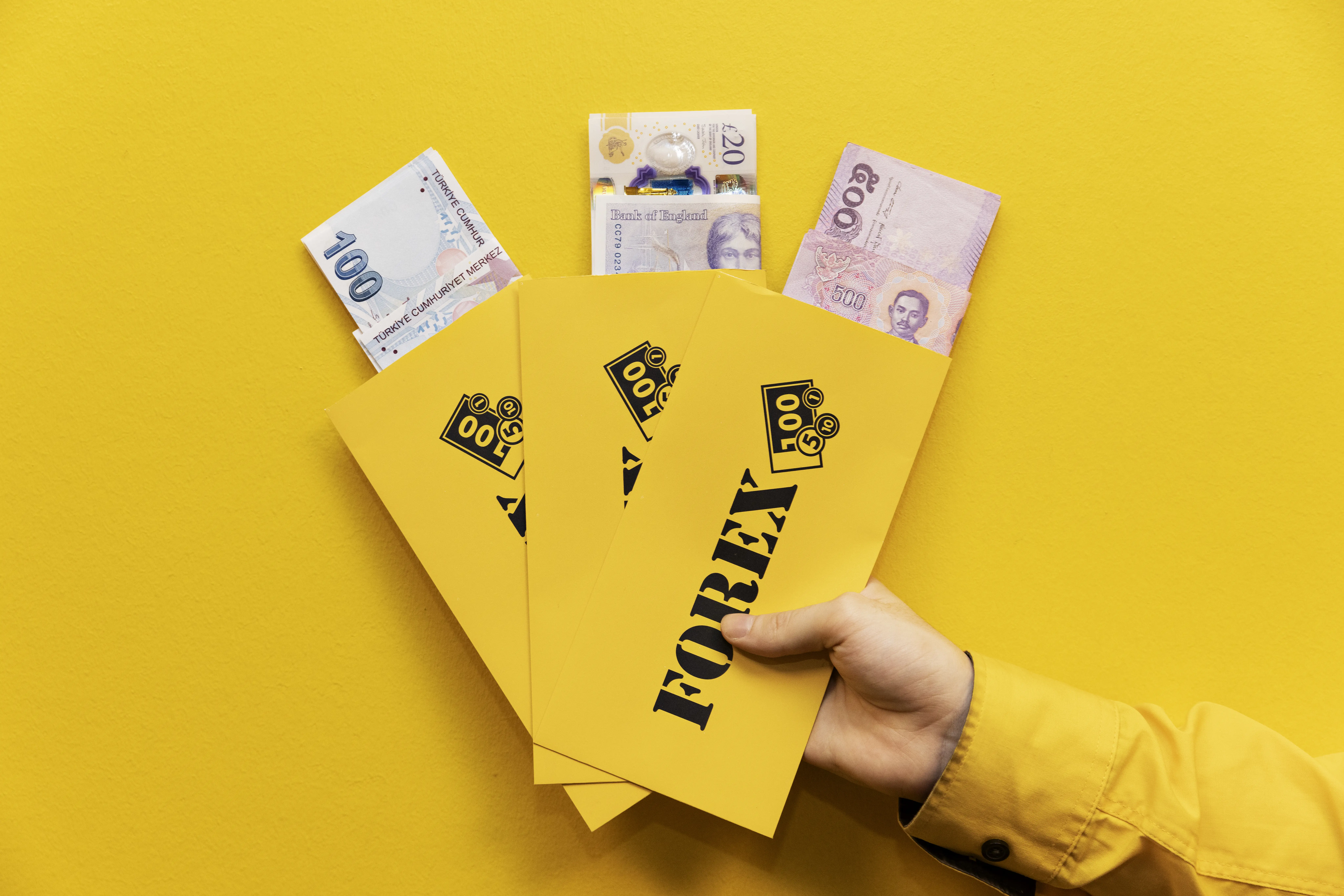Hand with yellow sleeve holding up three yellow FOREX envelopes with travel currencies for travel