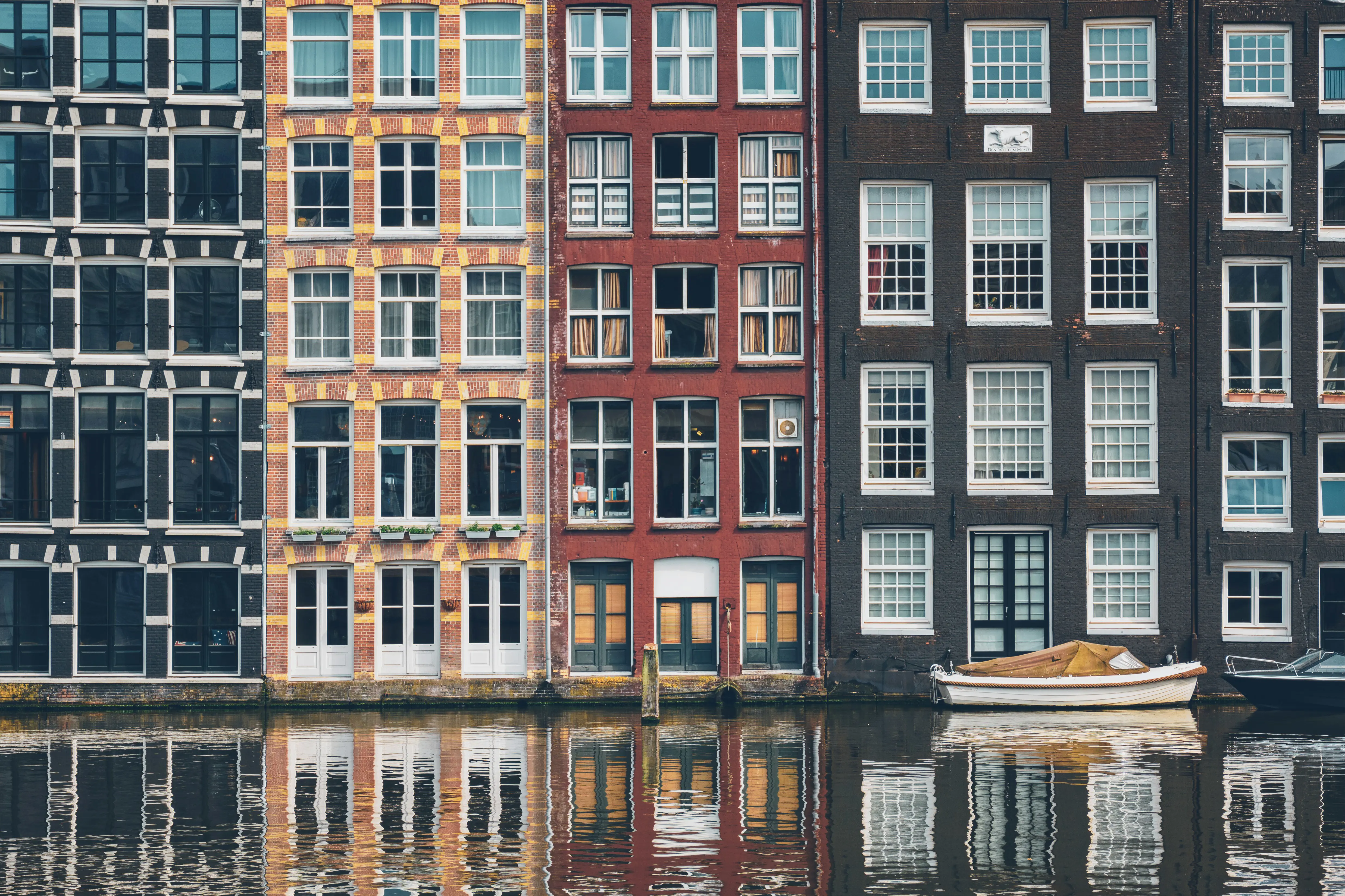 Kanalhus med fargerike fasader og store vinduer gjenspeiles i vannet i Amsterdam