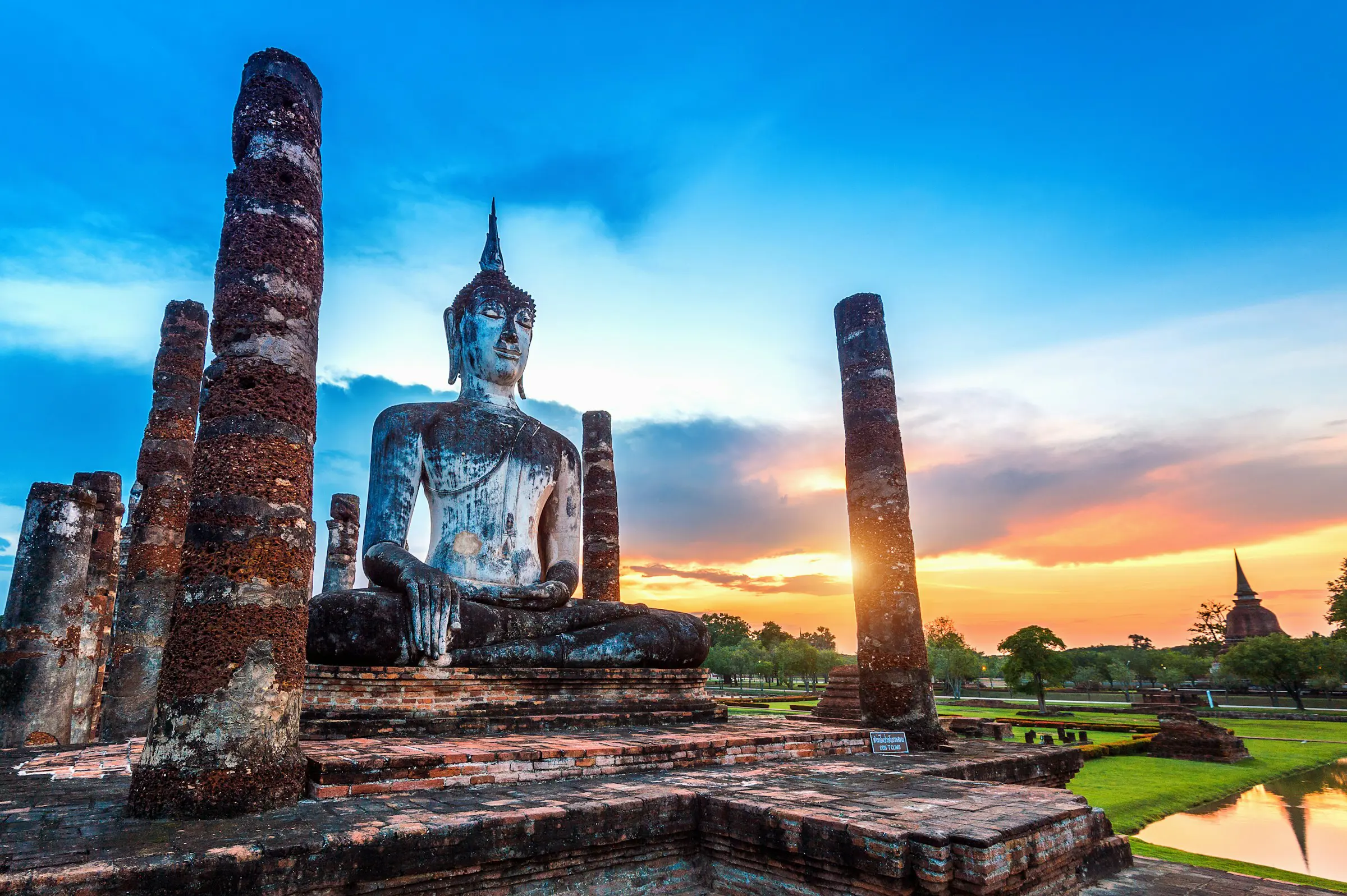 En Buddha-statue på en høyde omgitt av natur i skumringen i Thailand